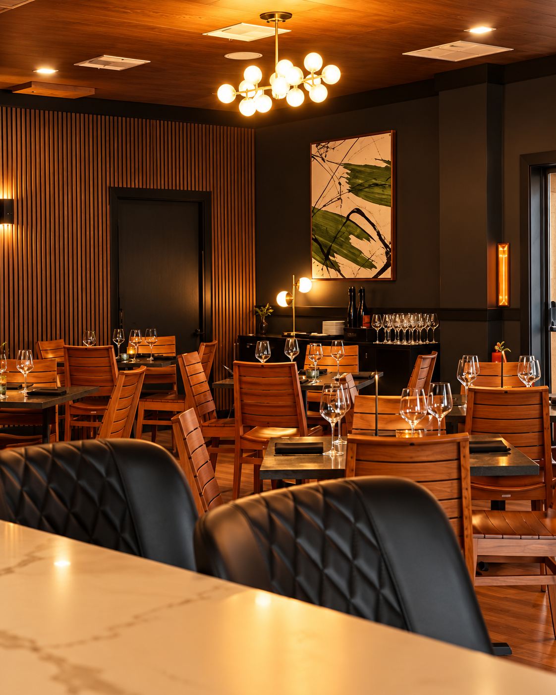 Dining area at Salt & Ember in Mount Dora with a wood slat wall, banquettes, and chandelier